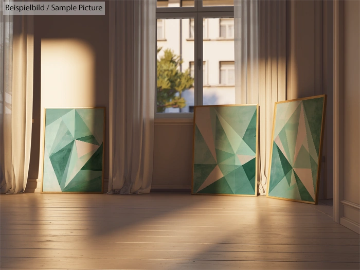 Three abstract teal and green geometric paintings leaning against a sunlit wall in a room with windows.