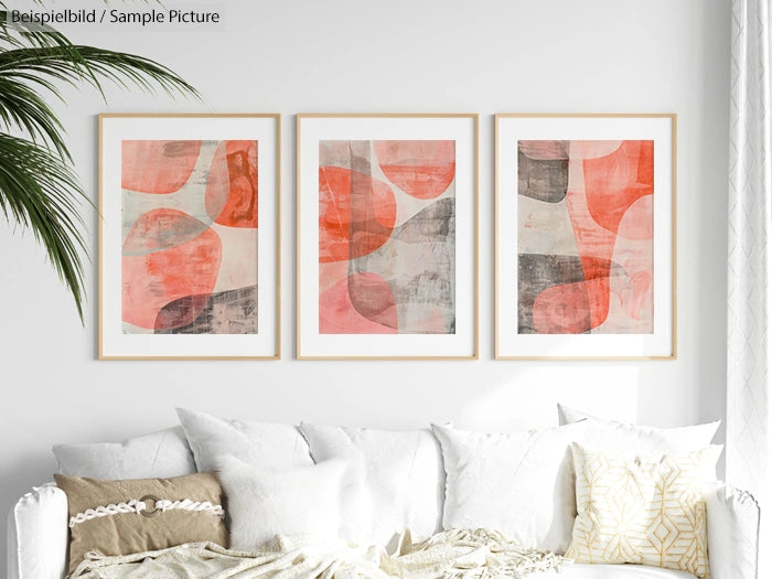 Trio of abstract art prints with red, beige, and gray tones, framed and hung above a white sofa with decorative pillows.