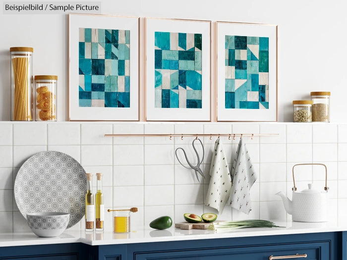 Modern kitchen with abstract art, white tiles, and blue cabinets. Three framed teal geometric prints above countertop.