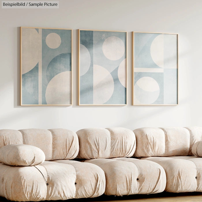 Modern living room with beige sofa and three geometric abstract paintings in soft blue and white tones on the wall.