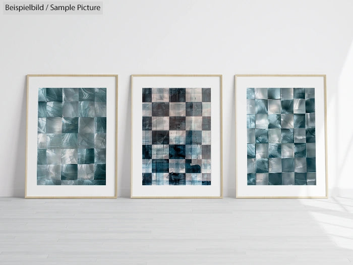 Three framed abstract mosaic art prints in blue, grey, and white hues on a white wall in a minimalist room.