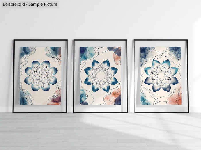 Three framed abstract mandala artworks with blue and orange hues displayed on a light wooden floor against a white wall.