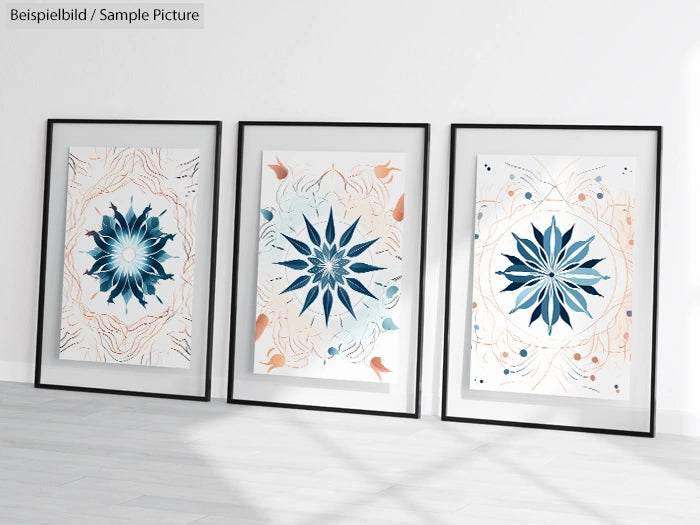 Three framed artworks with floral mandala designs in blue and beige on a white background, leaning against a wall.