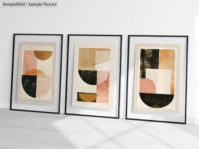 Three framed abstract geometric paintings with shades of pink, black, and beige, displayed on a wooden floor.