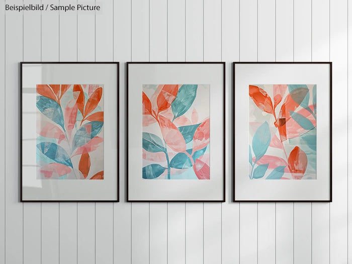 Three framed leaf art prints with orange and blue leaves on a white shiplap wall.