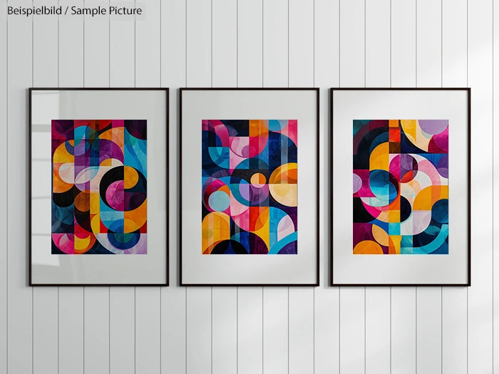 Three framed abstract paintings with geometric shapes in vibrant colors on a white paneled wall.