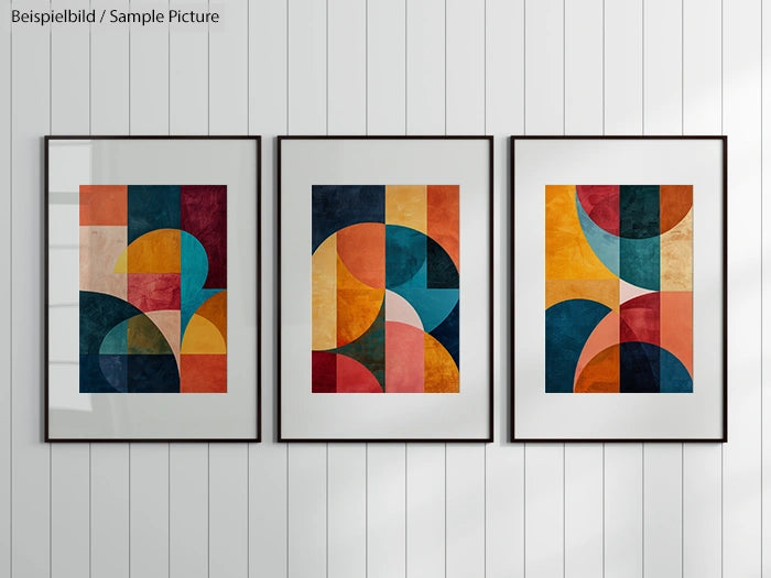 Three framed abstract geometric paintings with colorful arcs and shapes on a wood-paneled wall.