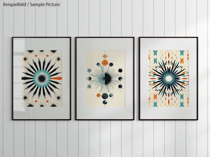 Three abstract starburst art prints in black frames on a white paneled wall.