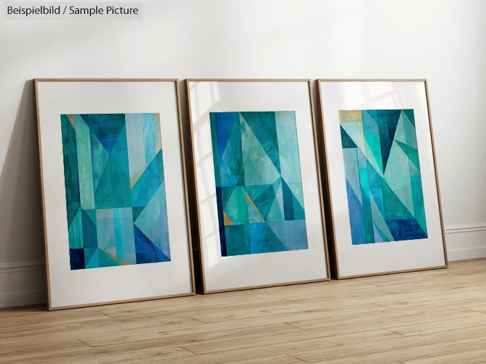 Three abstract blue and teal geometric paintings in frames on a wooden floor against a white wall.