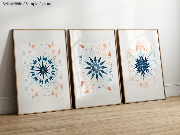 Three framed mandala illustrations with blue and tan accents, arranged on a wooden floor against a light wall.