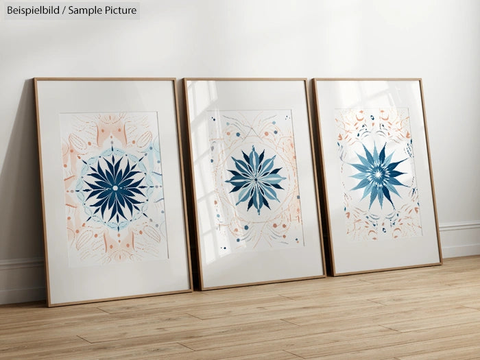 Three framed geometric floral prints in blue and peach tones on a wooden floor against a white wall.