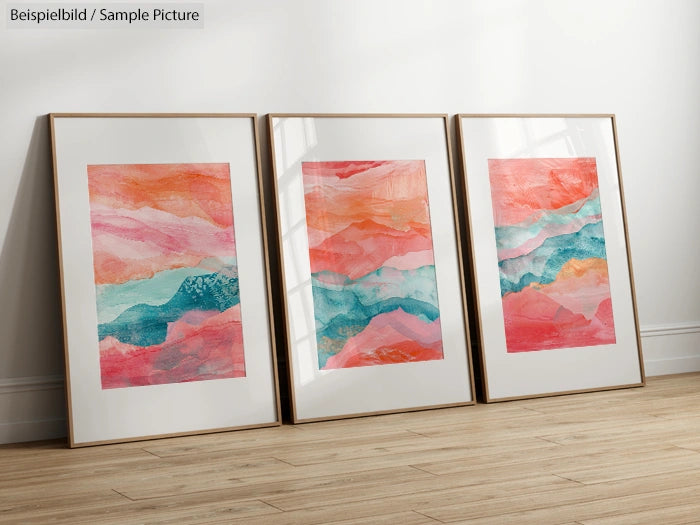 Three framed abstract paintings with pink, orange, and teal brushstrokes on a wooden floor against a white wall.