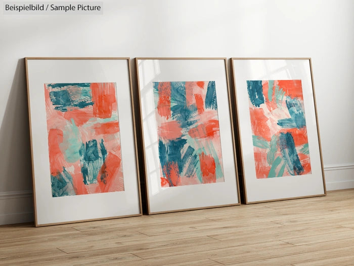 Three abstract paintings with red, teal, and white brush strokes in wooden frames on a wooden floor.