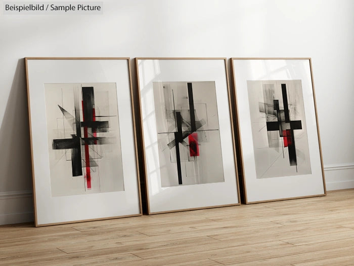 Three framed abstract paintings with black and red geometric shapes on a wooden floor.