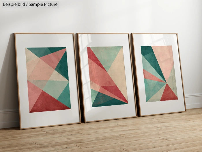 Three framed geometric abstract artworks with teal, pink, and beige triangles on a light wooden floor.