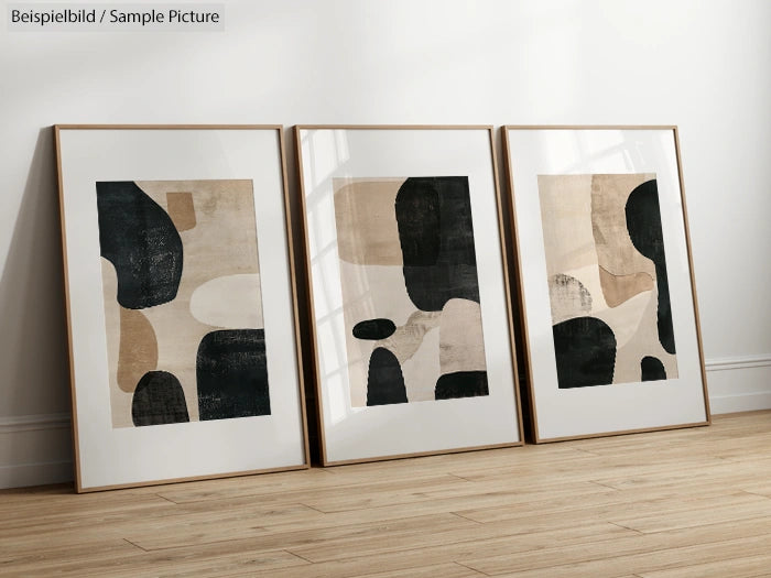 Three framed abstract paintings with black and beige geometric shapes, displayed on a wooden floor against a white wall.