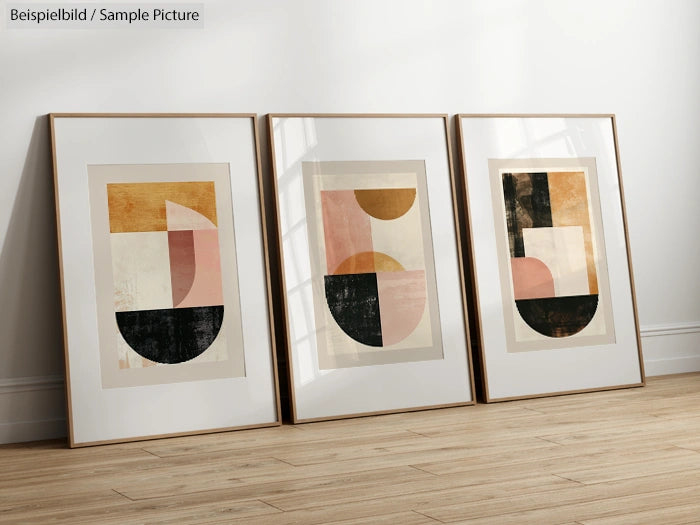 Three framed abstract art prints with geometric shapes in pastel and black tones, leaning on a wooden floor.