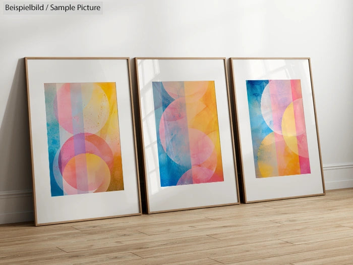 Three framed abstract art prints with colorful overlapping circles, leaning against a white wall on a wooden floor.