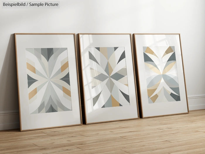 Three framed geometric abstract art prints with muted tones leaning against a white wall on a wooden floor.